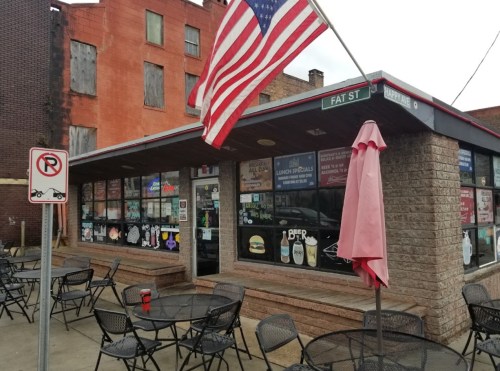 A small restaurant with outdoor seating, featuring an American flag and various signs on the windows.