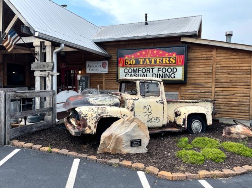 A vintage truck displayed outside a rustic restaurant named "50 Taters," featuring a sign for comfort food dining.