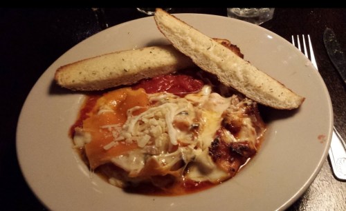 A plate of lasagna topped with melted cheese and sauce, accompanied by two slices of garlic bread.