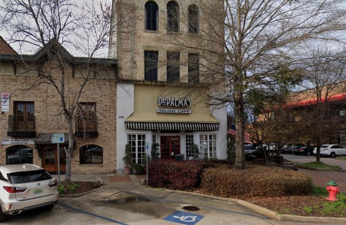 Exterior of DePalma's Italian Cafe, featuring a stone building with trees and parked cars in the foreground.