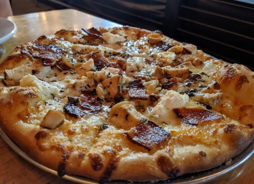 A freshly baked pizza topped with cheese, chicken, and crispy bacon on a golden crust.