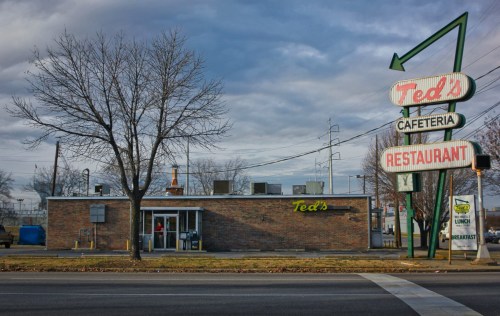 A brick restaurant with a retro sign reading "Ted's Cafeteria Restaurant" under a cloudy sky.