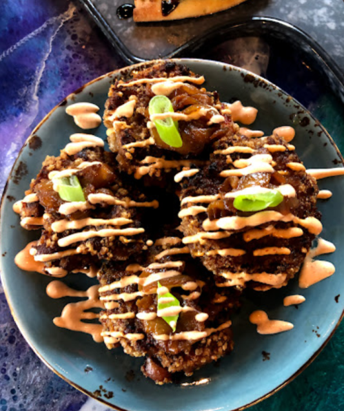 A plate of crispy fritters drizzled with sauce and topped with green onions, served on a colorful background.