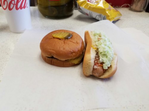 A hamburger with a pickle and a hot dog topped with lettuce and tomato, placed on a white paper surface.