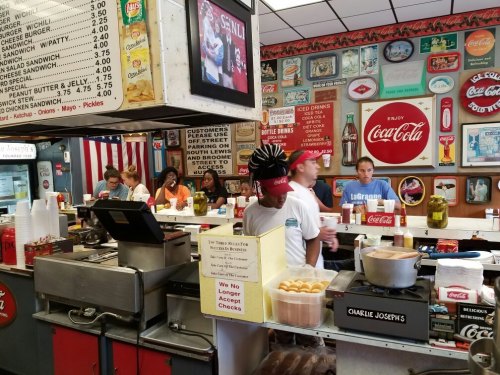 A busy diner with a retro vibe, featuring a counter, customers, and vintage Coca-Cola advertisements on the walls.