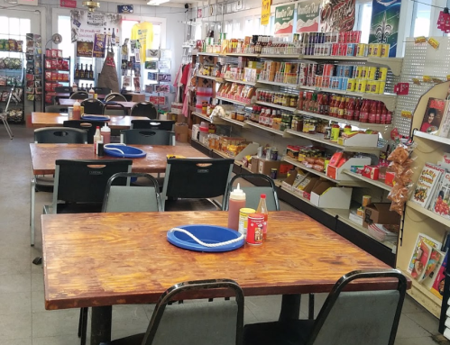 A cozy diner with wooden tables, condiment bottles, and shelves stocked with various food items.