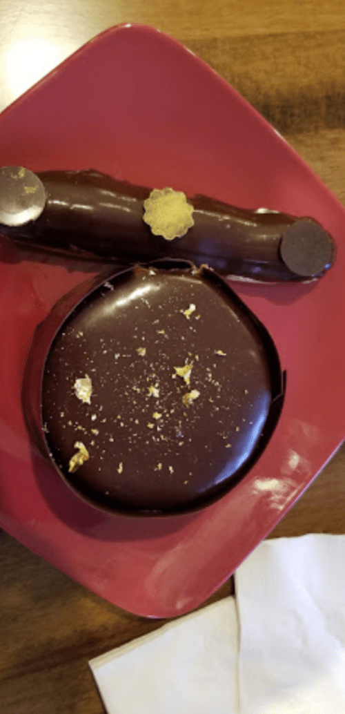 A round chocolate dessert with gold accents and a chocolate log on a red plate, set on a wooden table.