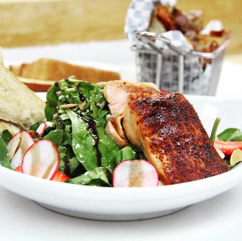 A plate of grilled salmon with a fresh salad, including spinach and radishes, served with slices of bread.
