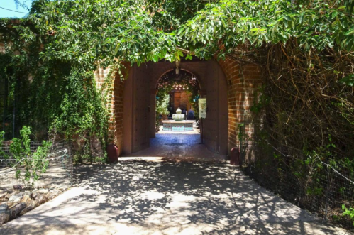 A serene garden entrance framed by lush greenery, leading to a tranquil courtyard with a fountain.