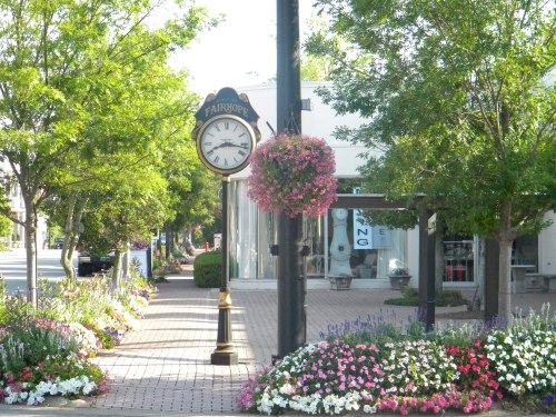 A charming street scene featuring a clock, hanging flower baskets, and colorful flower beds in a quaint town.