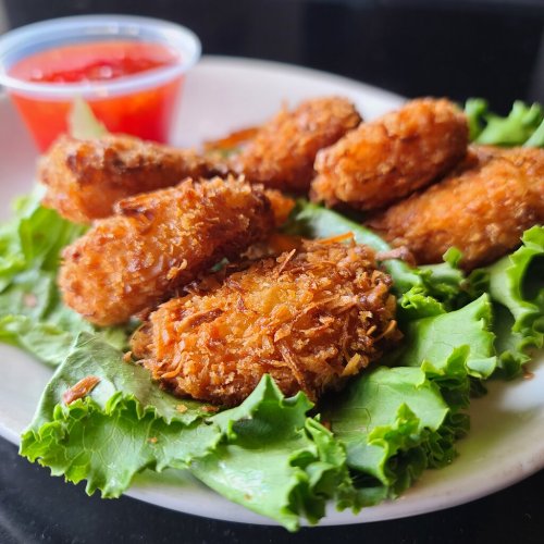 A plate of crispy fried chicken nuggets on a bed of lettuce, served with a small cup of dipping sauce.