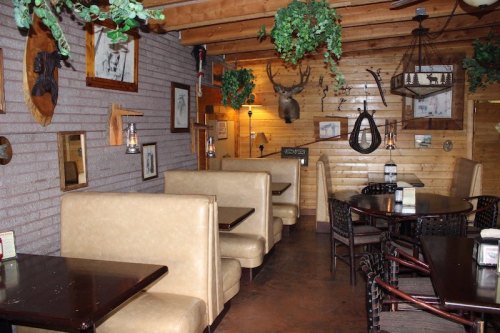 Cozy restaurant interior with wooden walls, booths, and rustic decor, including animal mounts and hanging plants.