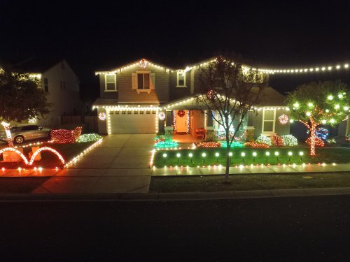 A house decorated with colorful holiday lights, featuring illuminated trees and a festive arch in the front yard.