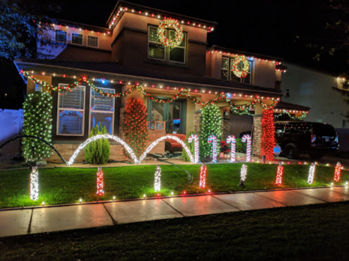A house decorated with colorful Christmas lights, featuring wreaths, candy canes, and festive greenery.