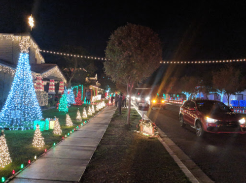 A festive street scene at night, adorned with colorful holiday lights and decorations along the sidewalk and houses.