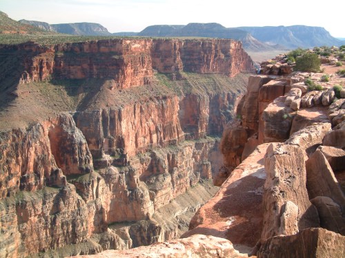 A vast canyon with steep, rocky cliffs and layered red rock formations under a clear sky.