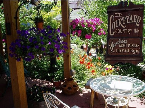 A charming garden patio with colorful flowers, a glass table, and a sign for "The Courtyard Country Inn."