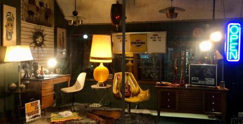 A vintage shop display featuring retro furniture, lamps, and a neon "OPEN" sign.