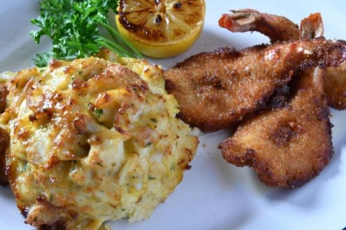A plate featuring crab cakes, fried shrimp, and a grilled lemon slice, garnished with parsley.