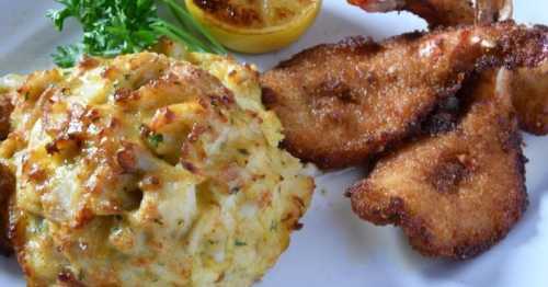 A plate featuring golden-brown fried fish, crab cakes, and a lemon wedge, garnished with parsley.