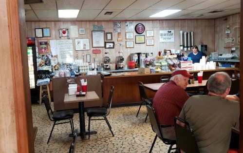 A cozy diner interior with wooden paneling, tables, and a counter displaying various signs and decorations.
