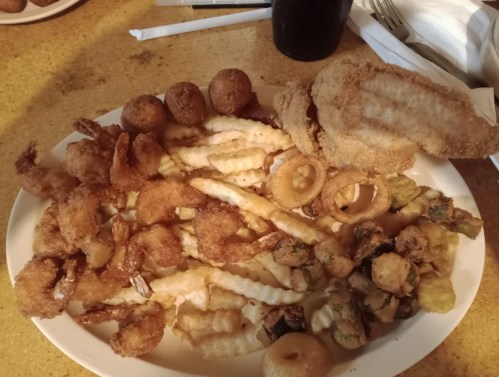 A large plate of assorted fried foods, including shrimp, fries, and hushpuppies, arranged appetizingly.