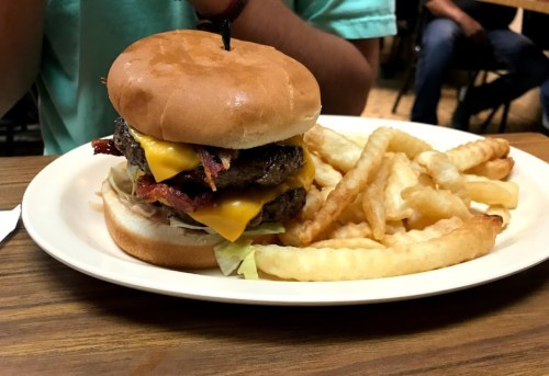 A large cheeseburger with bacon, lettuce, and a side of crinkle-cut fries on a plate.