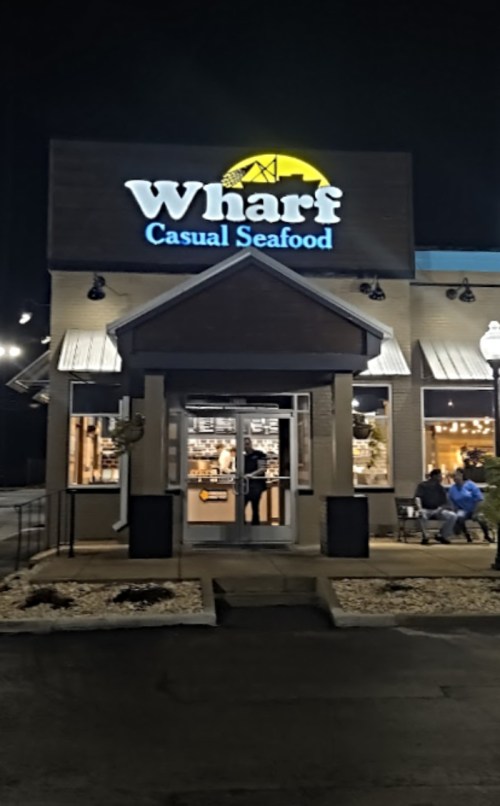 A seafood restaurant named "Wharf Casual Seafood" illuminated at night, with people seated outside.