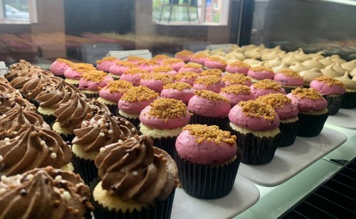 A display of colorful cupcakes with chocolate and pink frosting, topped with crumbs and sprinkles.