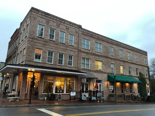 Historic brick building with large windows, featuring a storefront and awning, on a rainy evening.