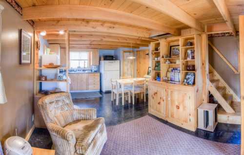 Cozy wooden interior of a cabin with a living area, kitchen, dining table, and staircase. Warm, inviting atmosphere.