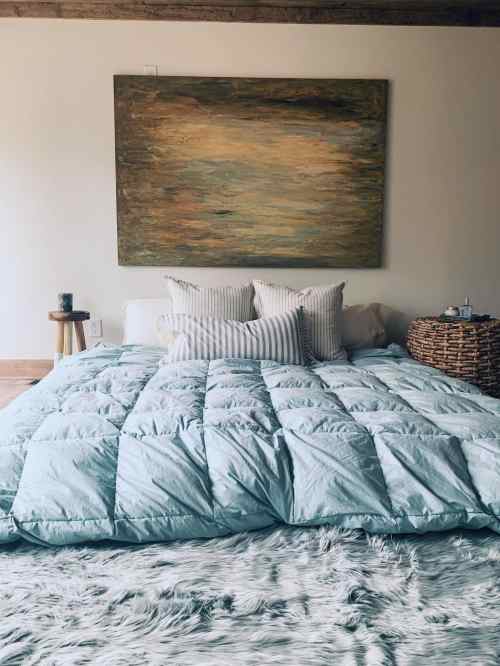 A cozy bedroom featuring a large bed with a light blue comforter, decorative pillows, and a textured rug.