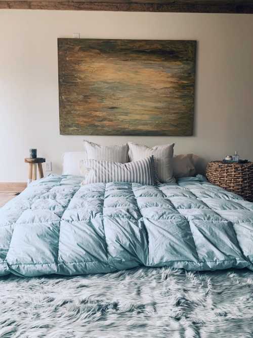 A cozy bedroom featuring a large bed with a light blue comforter, decorative pillows, and a textured rug.