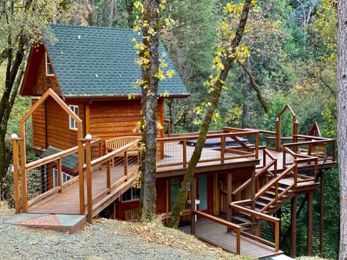 A wooden cabin with a green roof, surrounded by trees, featuring a large deck and multiple walkways.