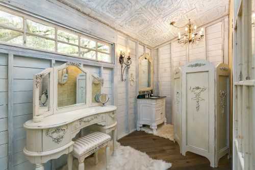 A vintage-style bathroom with a white vanity, ornate mirrors, and elegant decor, featuring soft rugs and natural light.