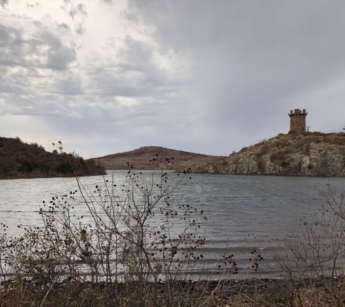 A serene landscape featuring a lake, rocky hills, and a distant tower under a cloudy sky.