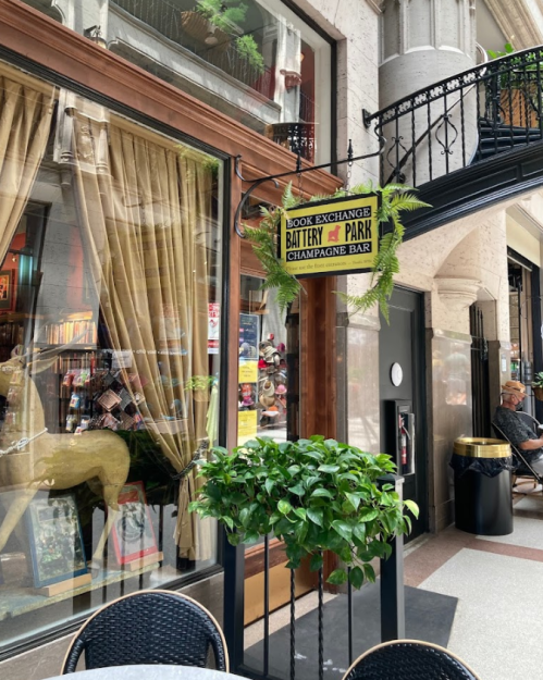 A cozy outdoor seating area near a book exchange and champagne bar, with plants and elegant decor.