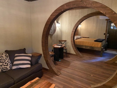 Cozy room featuring circular wooden arches, a sofa, a bed, and warm lighting in a rustic setting.