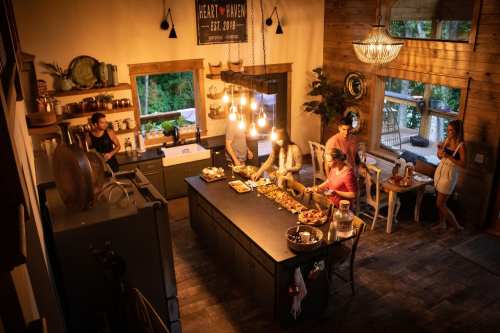 A cozy kitchen scene with people preparing food, warm lighting, and a welcoming atmosphere.