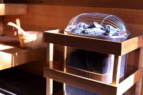 A wooden sauna interior featuring a charcoal stove and a wooden bucket on a shelf.