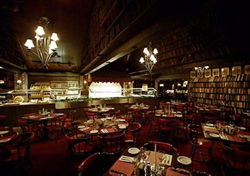 Cozy restaurant interior with wooden bookshelves, round tables, and warm lighting, creating an inviting atmosphere.