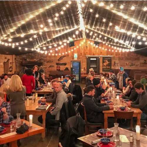 A cozy restaurant interior with string lights, featuring diners at long tables enjoying their meals.