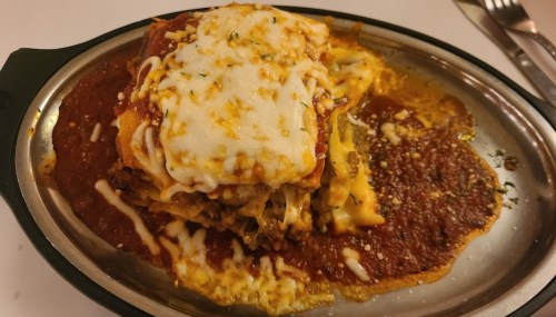 A serving of lasagna topped with melted cheese, served in a metal dish with marinara sauce.