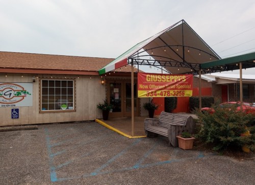 Exterior of Giusseppi's restaurant with a colorful awning and a sign advertising specials. Parking area visible.