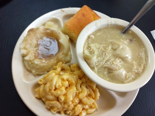 A plate with mashed potatoes, chicken and dumplings, macaroni and cheese, and a piece of cornbread.