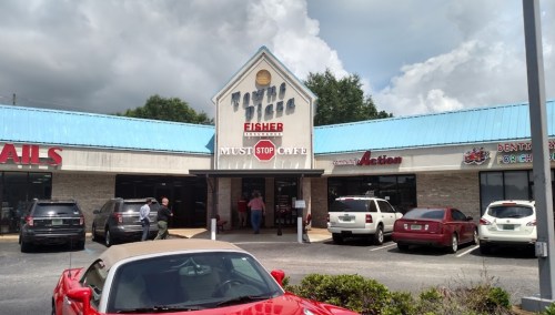 A storefront with a blue roof, featuring "Must Stop Café" and "Fisher" signage, with cars parked outside.