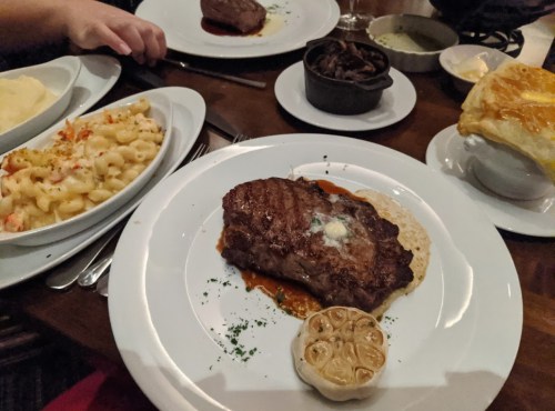 A plate featuring a steak with sauce, a side of mashed potatoes, macaroni and cheese, and a small pastry.