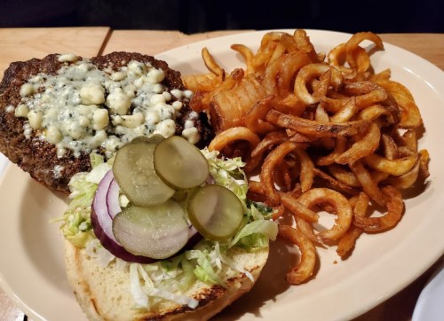 A plate featuring a blue cheese burger with pickles and lettuce, alongside curly fries.
