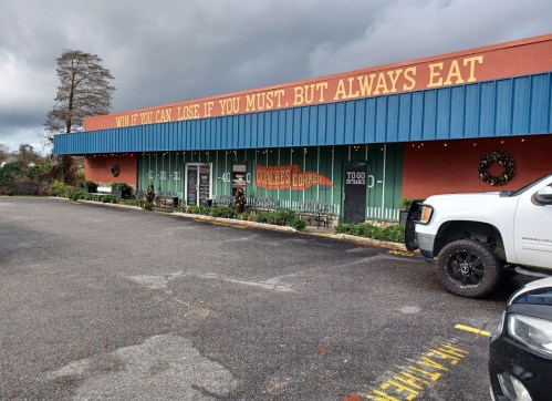 A restaurant exterior with a colorful sign reading, "Win if you can, lose if you must, but always eat."