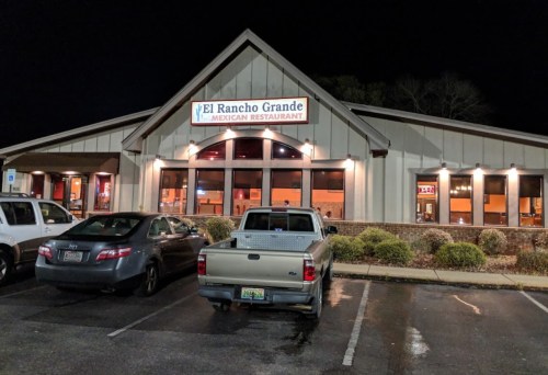 Exterior of El Rancho Grande Mexican Restaurant at night, featuring a large sign and parked cars in front.